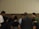 A group of people standing in a circle, appearing to be engaged in a moment of reflection or prayer. The setting is indoors with a neutral-colored background.