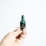 A hand holding a small chocolate in the shape of a miniature bottle, wrapped in green foil with a label that reads Rémy Martin Fine Champagne Cognac. The background is plain and white, highlighting the focus on the miniature chocolate bottle.