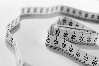 A coiled white measuring tape lies on a plain surface, displaying numbers and black markings clearly on the visible side.