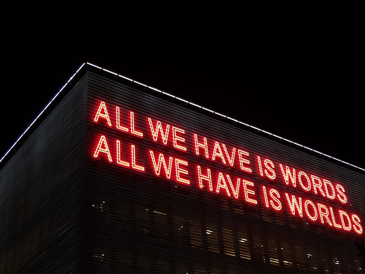 sign in the side of a building saing "All we have is words, all we have is worlds"