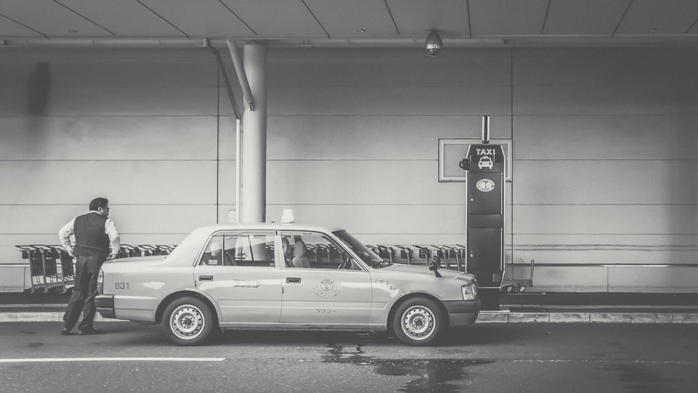 grayscale photo of man beside car