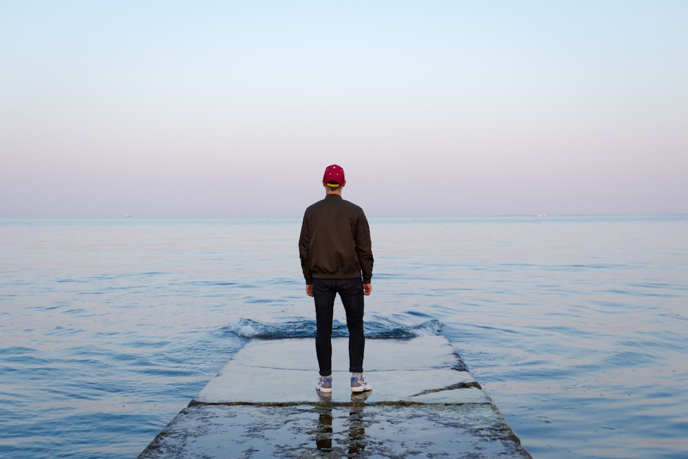 man standing on concrete dock facing sea