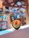 A tin of hair product from Nature Republic with argan oil is prominently displayed, resting on a white surface. The background is blurred but appears to be a colorful, warm-toned space with bookshelves and various items.