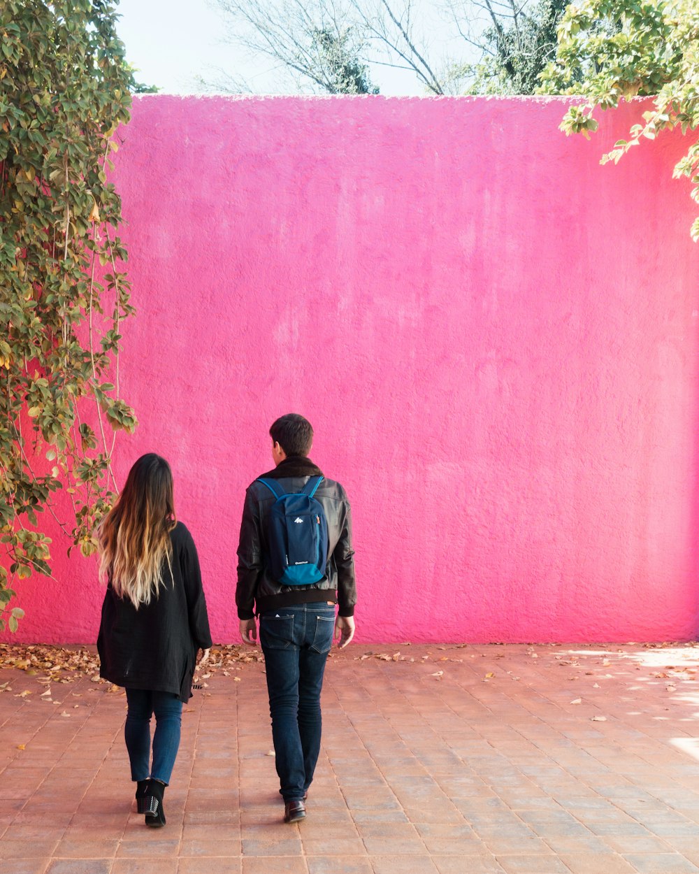 昼間、ピンクの壁のそばに立つ男女