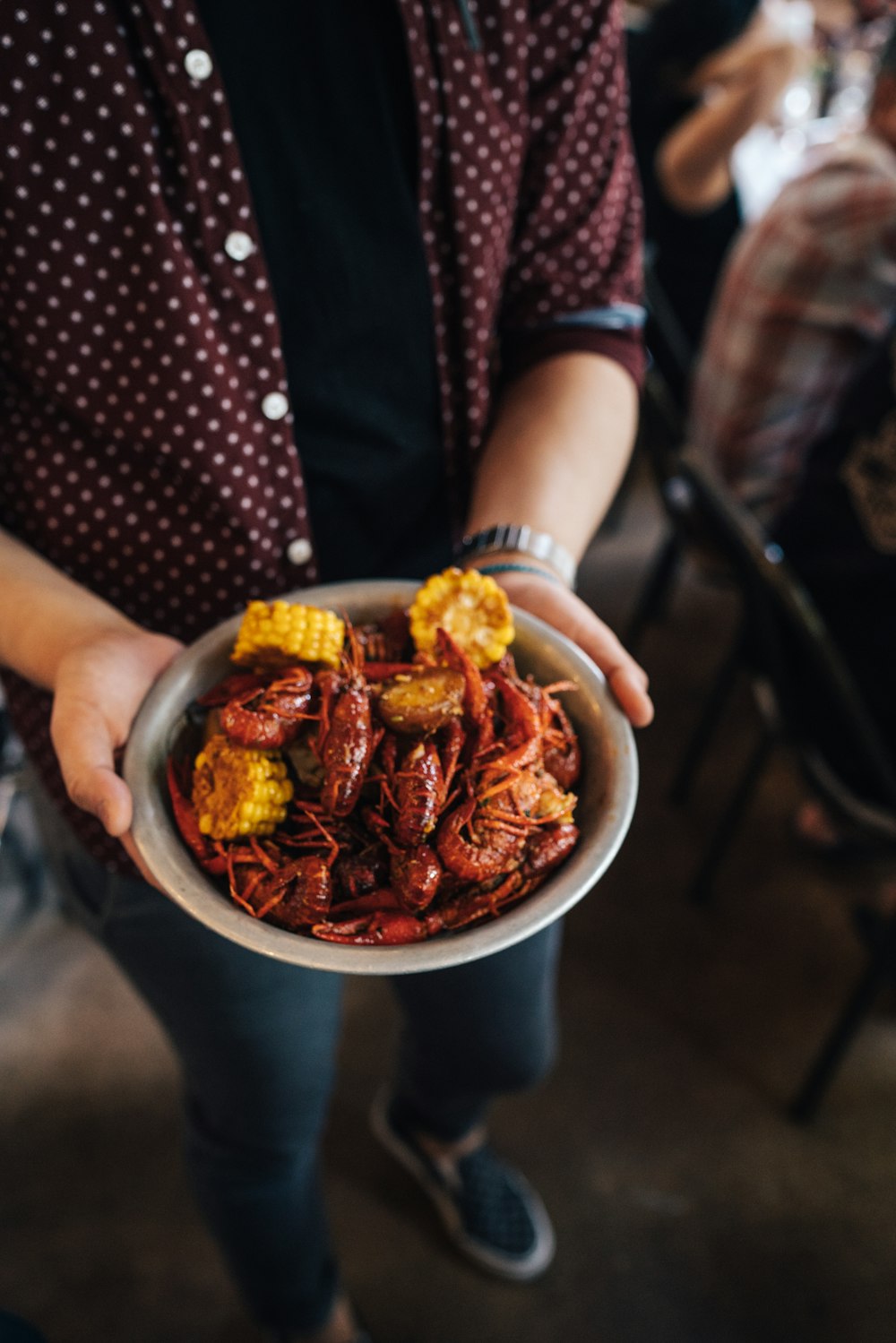 person holding bowl of shrimp with slice of corn dish