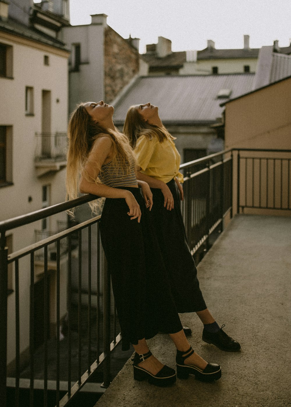 two women looking up white leaning on fence