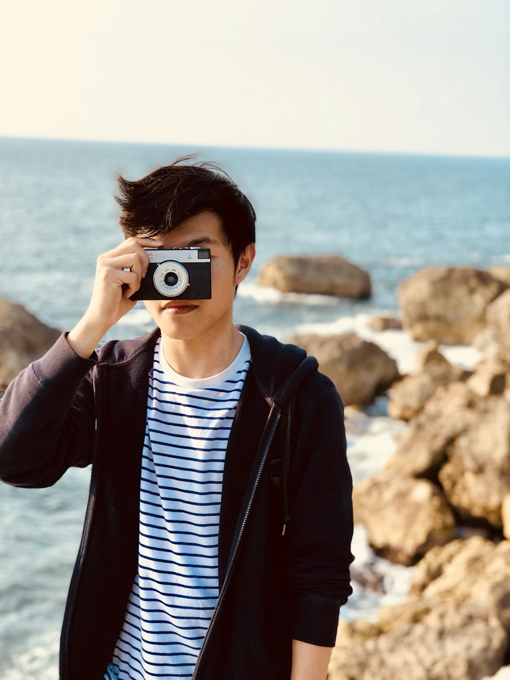 海の近くで灰色のオートフォーカスカメラで写真を撮る人