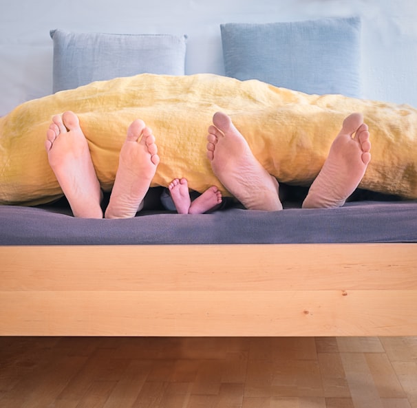 three people underneath yellow bed blanket