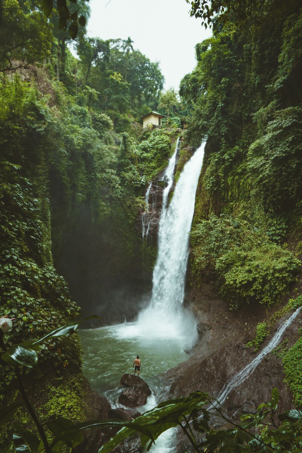 man standing on top of rock near waterfalls