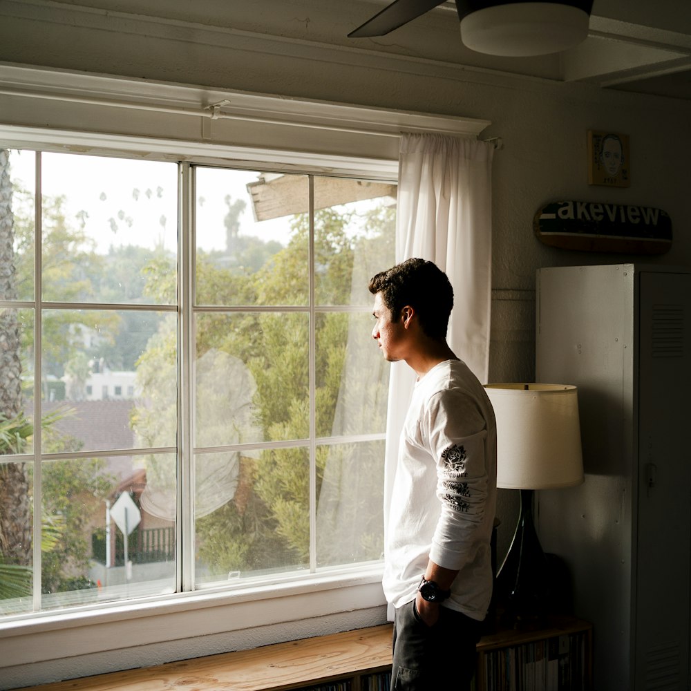 Hombre con camisa gris y negra de cuello redondo de pie y mirando por la ventana