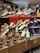 A display of various sneakers on top of stacked shoeboxes with a bustling crowd in a retail environment. The sneakers include colorful and patterned designs from Nike, with distinct animal prints and vibrant color schemes. Many people are in the background, some browsing the display.