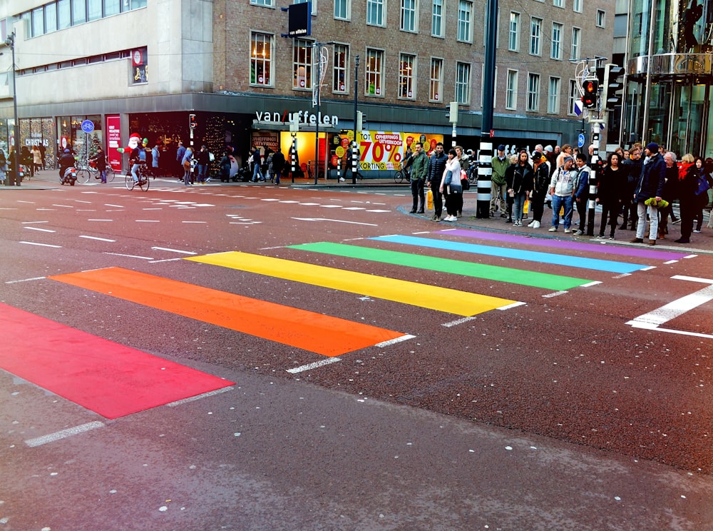 personas paradas en la carretera frente a una línea peatonal multicolor