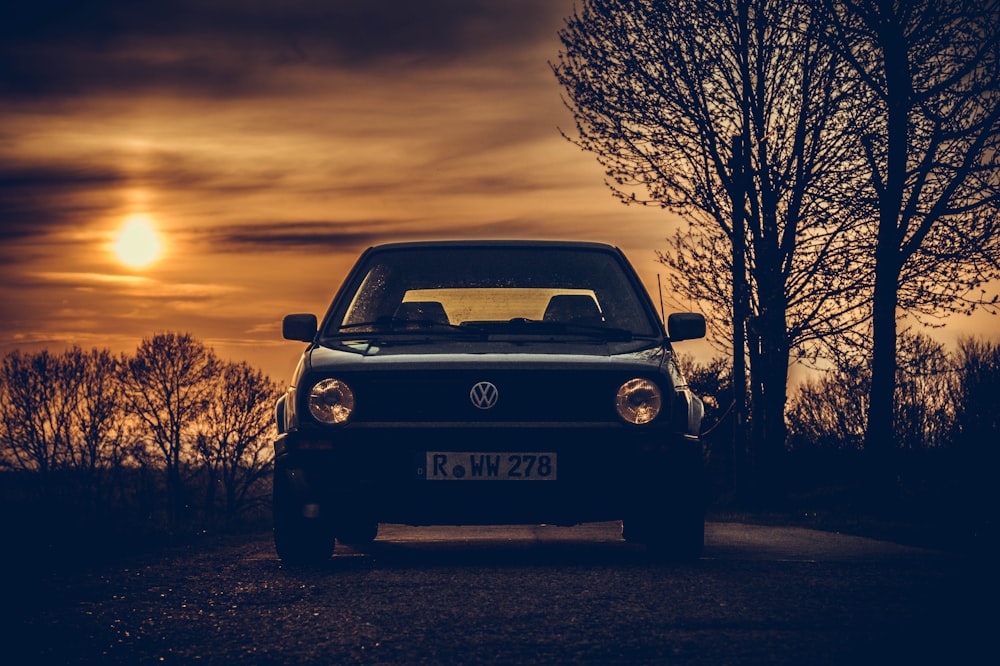 black Volkswagen vehicle in road beside bare trees at golden hor