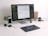 A modern workspace featuring a large monitor displaying a color palette application. Below the monitor, a keyboard and a graphics tablet with a stylus are present. A smartphone stands upright in a dock on the left next to a small potted plant. In the background, a wooden folder holder and a mug with text are visible. A stack of magazines or documents lies flat nearby.
