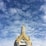 A temple roof with intricate golden details and traditional architectural design against a backdrop of a partly cloudy sky.