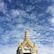 A temple roof with intricate golden details and traditional architectural design against a backdrop of a partly cloudy sky.