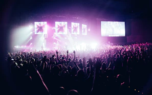 A glowing crowd bathed in deep purple and neon lights, hands raised at a Venus Live concert