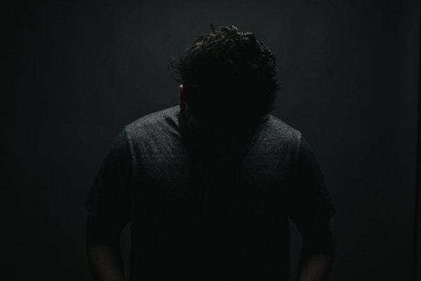 A moody, shadow-rich photograph focusing on the silhouette of a figure against a minimalist backdrop.