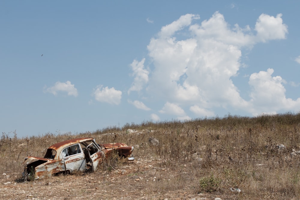 photo of wrecked sedan on brown grass field under clear blue sky