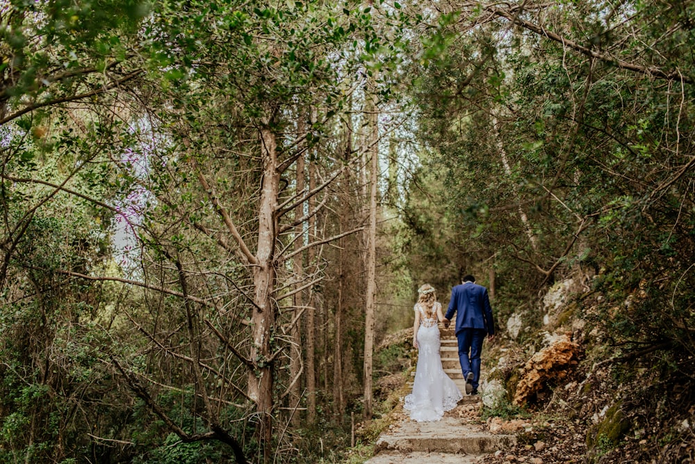 a bride and groom walking down a path in the woods