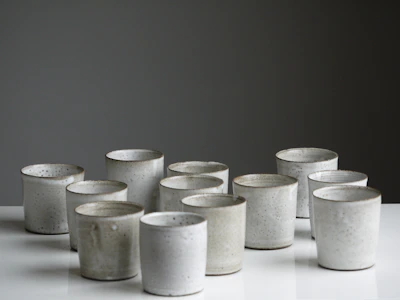 Close-up of small ceramic cups with earthy tones lined up on a smooth linen cloth.