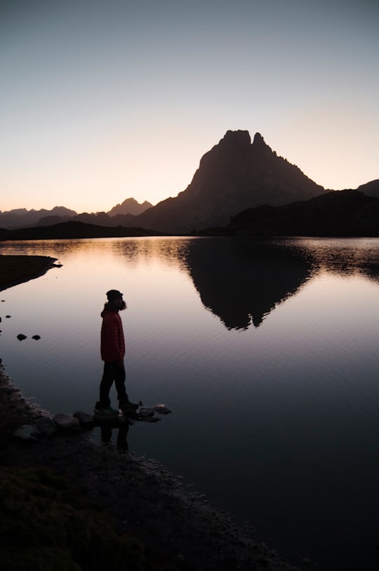 silhouette of person standing beside body of water near mountain during golden hour in Pic du Midi d'Ossau France