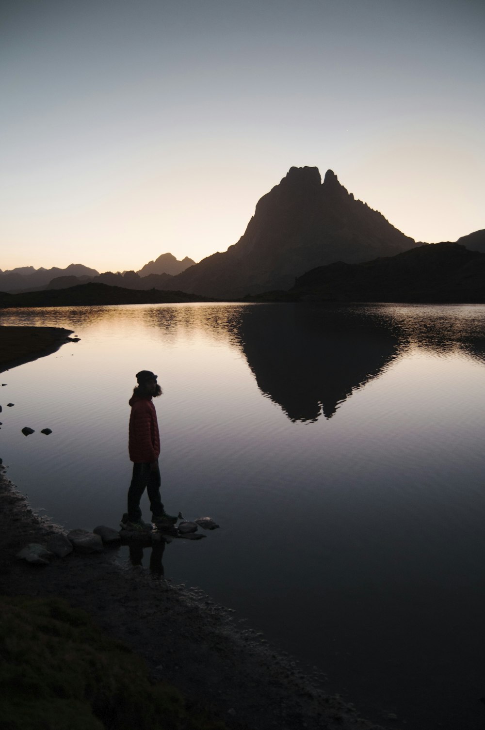 silhouette of person standing beside body of water near mountain during golden hour