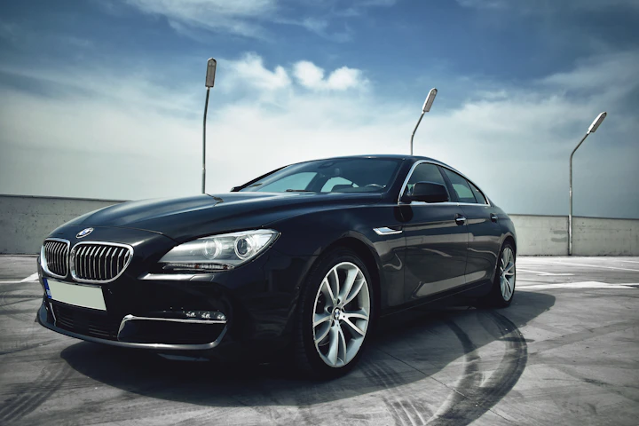 Front three-quarter view of a black BMW sedan on a concrete rooftop with circular tire skid marks and a blue sky