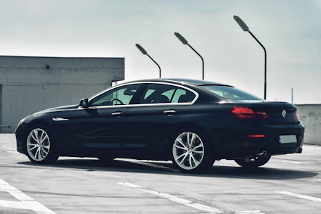 A sleek black luxury sedan parked curbside with city skyline at dusk.