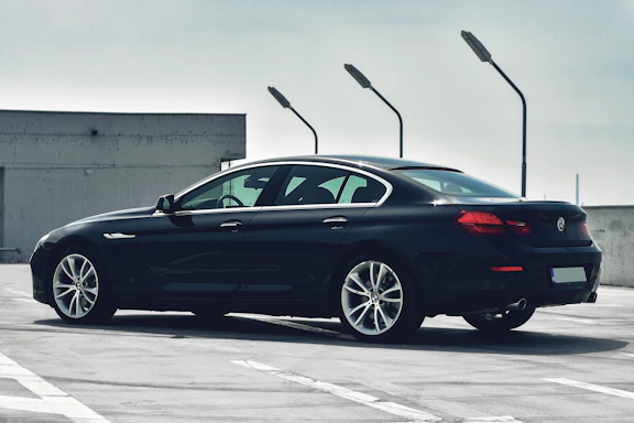 A sleek black luxury sedan parked in front of a modern Dubai skyscraper at sunset.
