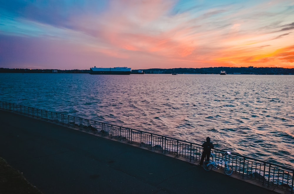 person standing on road in front of ocean during sunset