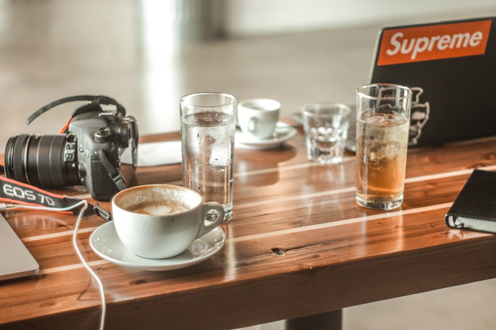 white teacup near Canon EOS 7D camera on brown wooden table