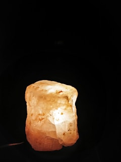 A large, translucent rock salt lamp is illuminated from within, casting a warm and soothing glow. The surface is rough and the color ranges from white to pale orange with scattered darker spots.