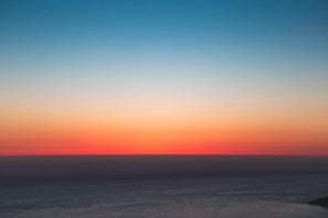 Blue ocean horizon blending into a sunset sky with orange and sand tones
