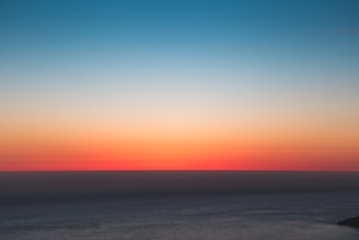 Blue ocean horizon blending into a sunset sky with orange and sand tones