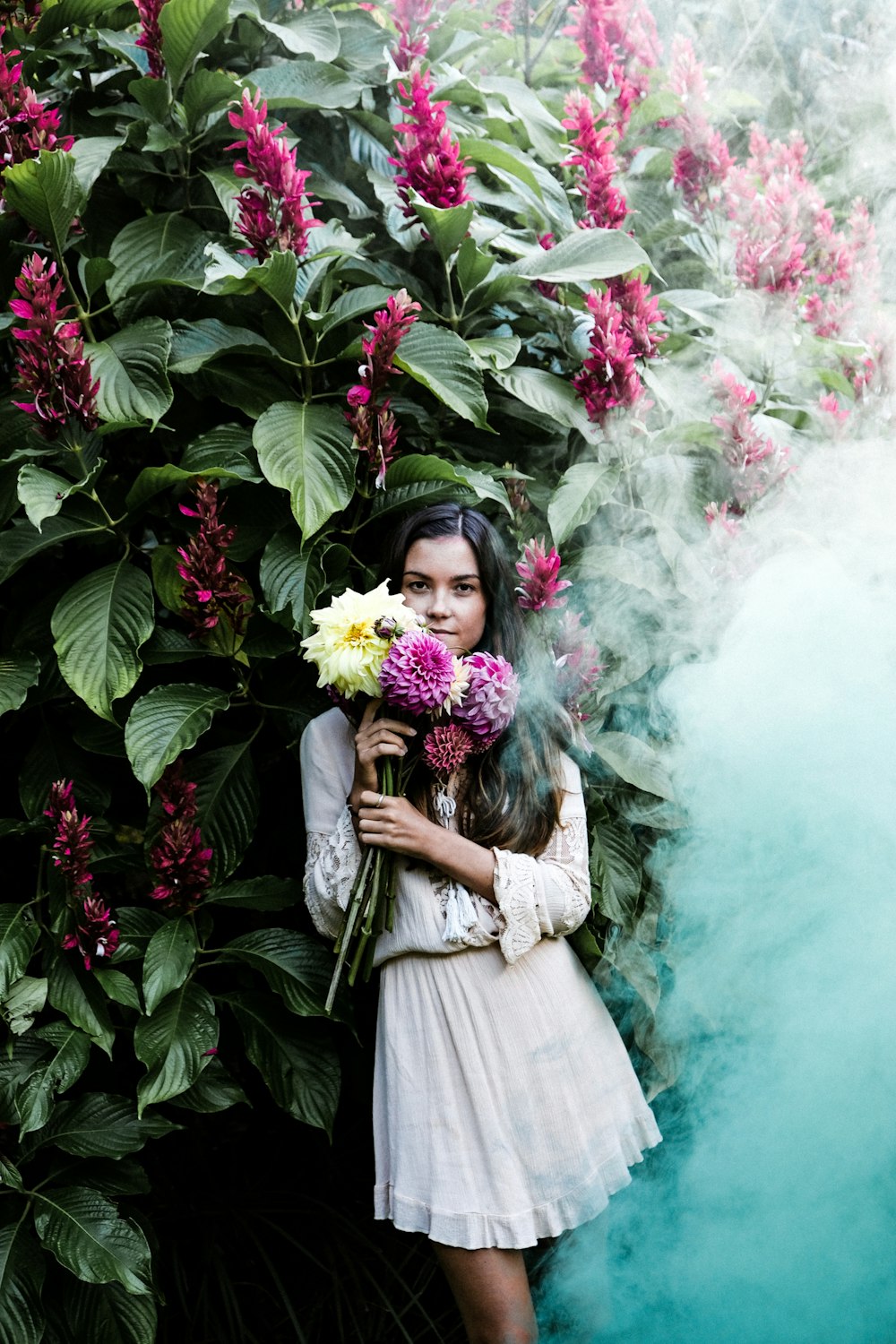 woman holding yellow and purple flowers leaning back on green leafed plants with flowers