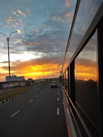 A vibrant tour bus driving along a scenic coastal road at sunset.