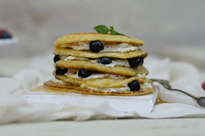 Stack of fluffy pancakes drizzled with maple syrup and dotted with juicy blueberries