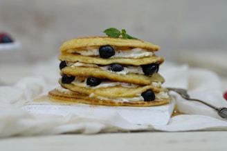 A stack of golden pancakes drizzled with maple syrup and dotted with blueberries.