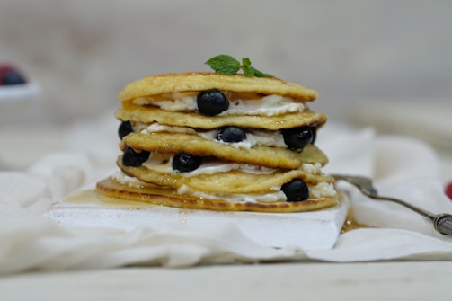 A stack of golden pancakes drizzled with maple syrup and dotted with blueberries.