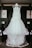 A white wedding dress with lace details is hanging on a wooden frame in a room. The dress has a full tulle skirt and intricate lace bodice, creating an elegant and romantic appearance.