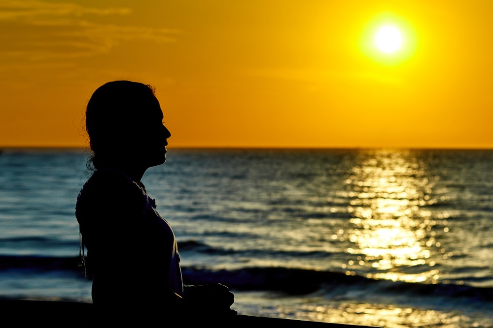 mulher em pé em frente à praia durante o pôr do sol