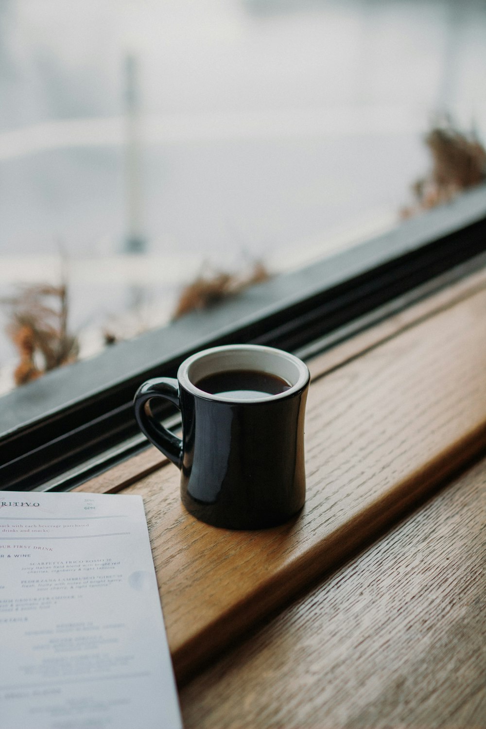 Photographie à mise au point peu profonde d’une tasse de café à côté d’une fenêtre en verre