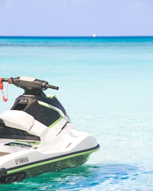 A jet ski, branded Yamaha, floating on clear turquoise water against a backdrop of a calm, blue ocean. The image captures the sleek design of the watercraft and the peacefulness of the surrounding seascape.