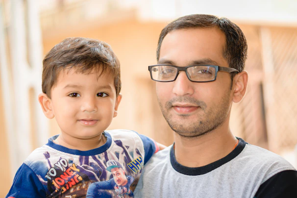 A happy father holding his child's hand as they both wear colorful eyewear after an eye exam.