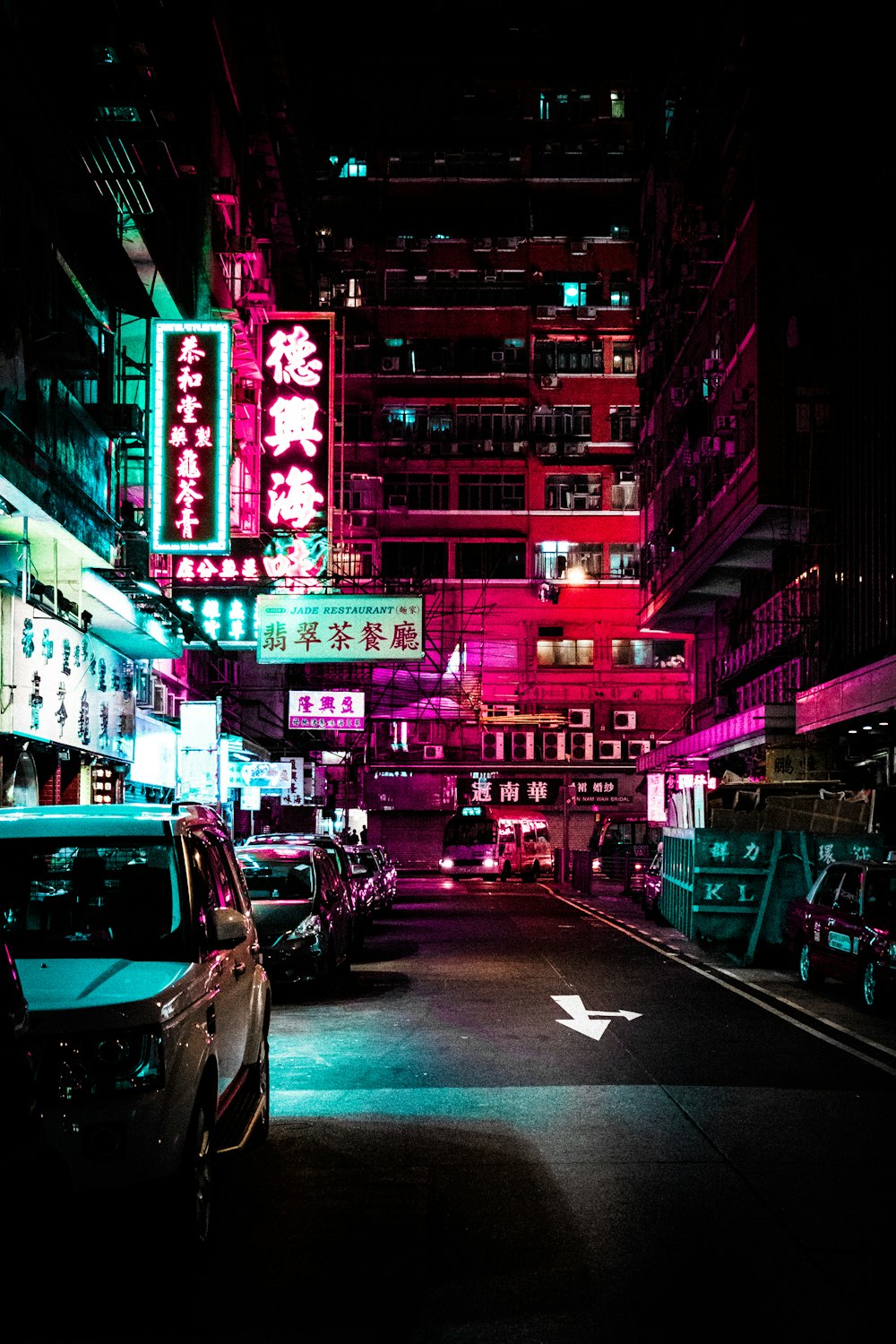 vehicles park on roadway between lighted buildings during nighttime