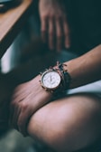Close-up of a brown leather watch and bracelet on a wrist, resting on ivory fabric.