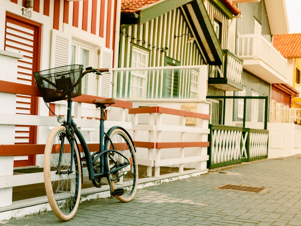 bicicleta preta e branca inclinada perto da cerca de madeira branca perto da casa durante o dia
