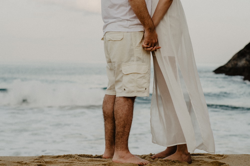 man and woman standing on seashore while holding hands