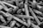 A pile of metallic spikes with rough surfaces, characterized by pointed ends and flat, wide heads. The image is presented in black and white, accentuating the texture of the metal.